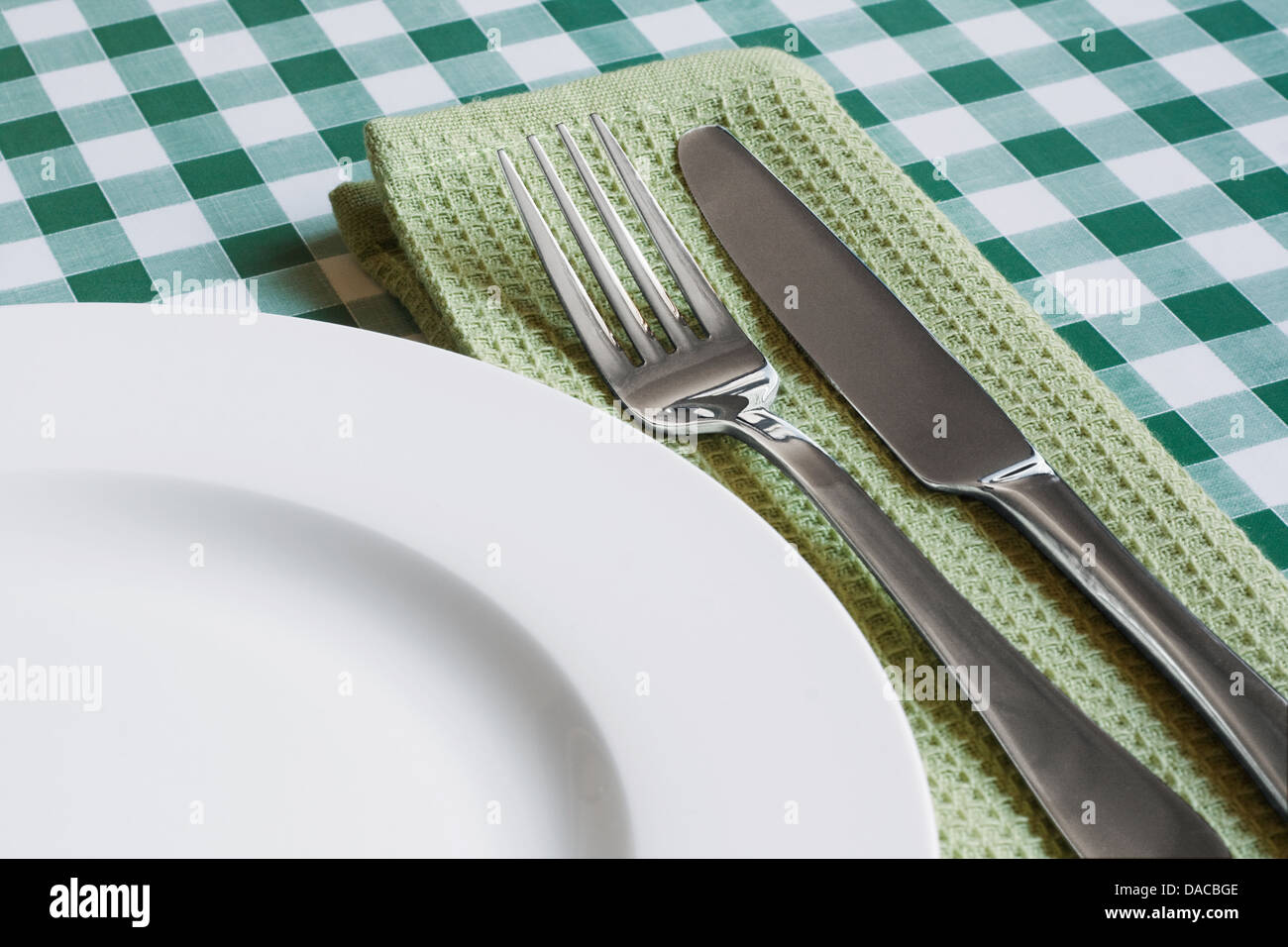 Posizionare l'impostazione con la piastra a vuoto, il coltello e la forchetta su un verde sfondo gingham simboli popolari per diners e caffè Foto Stock