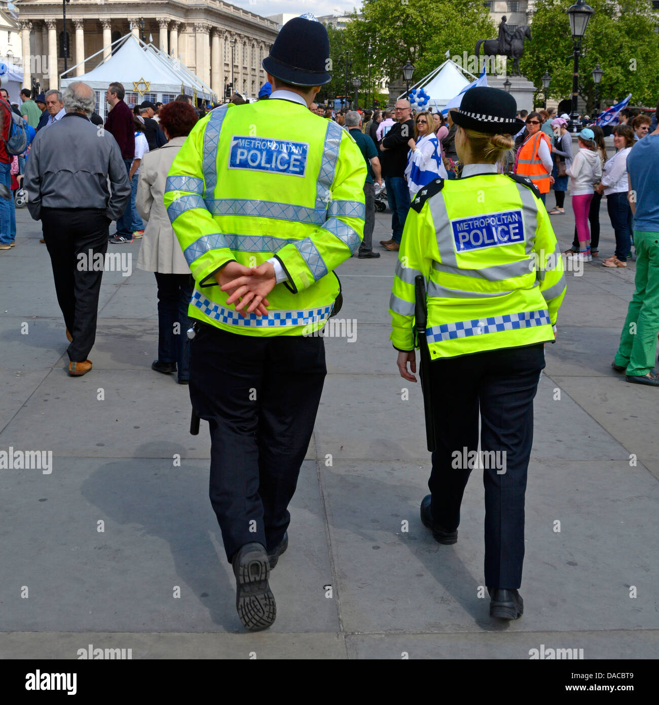 Vista posteriore maschio e femmina in uniforme WPC poliziotto sulla pattuglia a piedi in giacche ad alta visibilità pattugliando Trafalgar Square Londra Inghilterra UK Foto Stock