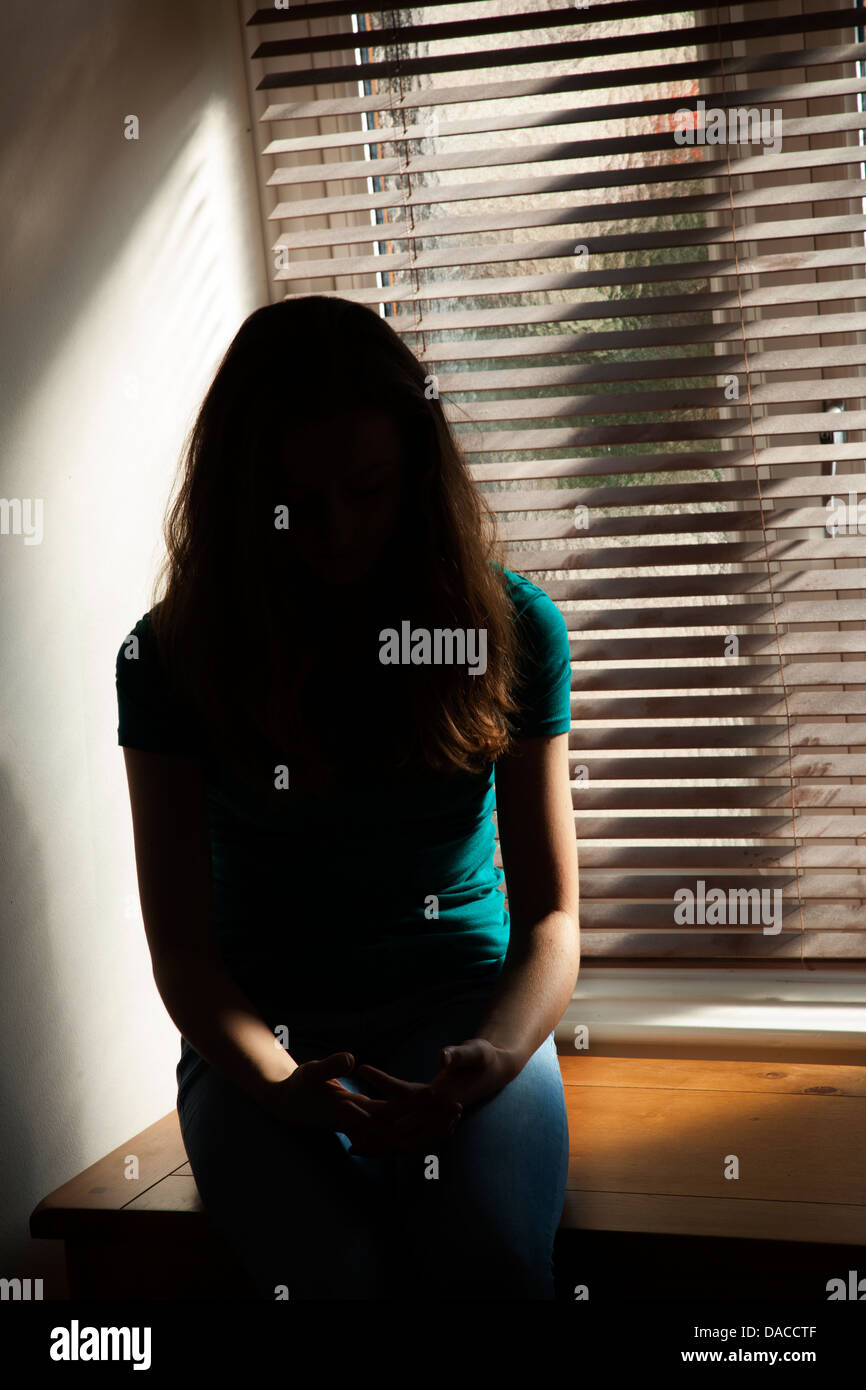 Una silhouette di una ragazza adolescente, seduti in una finestra. Foto Stock
