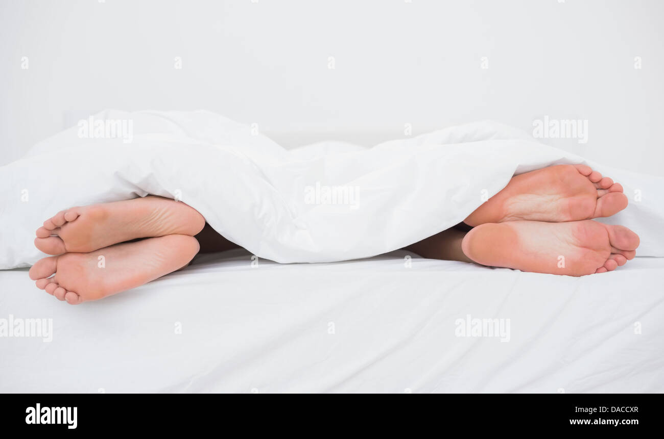 Piedi di coppia sui loro lati opposti a letto Foto Stock