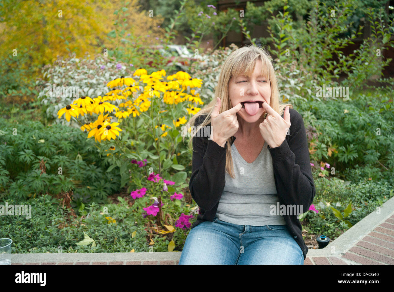 Donna seduta davanti a fiori facendo una buffa faccia. Foto Stock