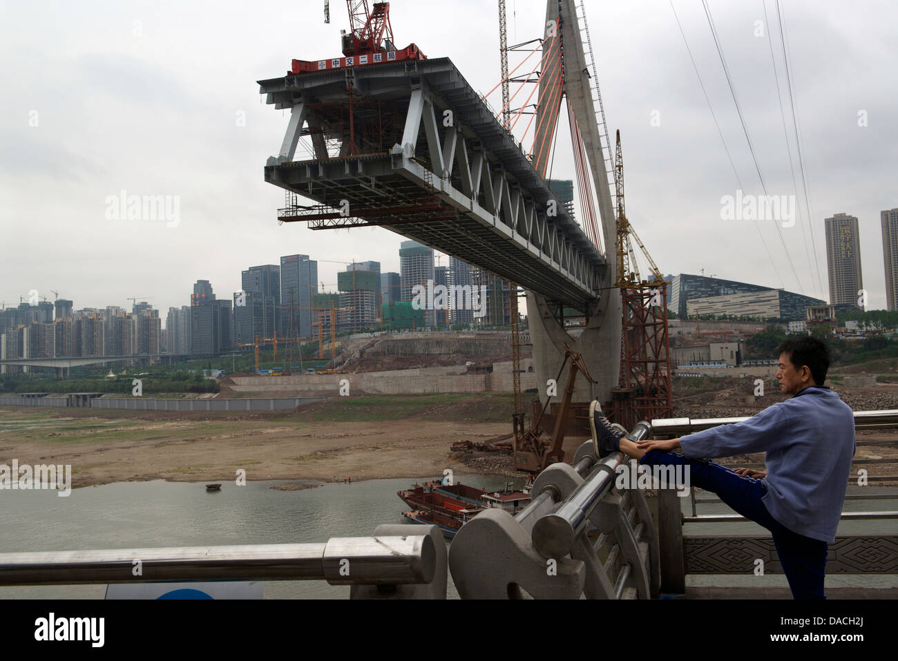 Un uomo fa esercizi del mattino nei pressi del ponte Qiansimen sotto costruzione sopra il fiume Jialing a Chongqing Cina. 08-Maggio-201 Foto Stock