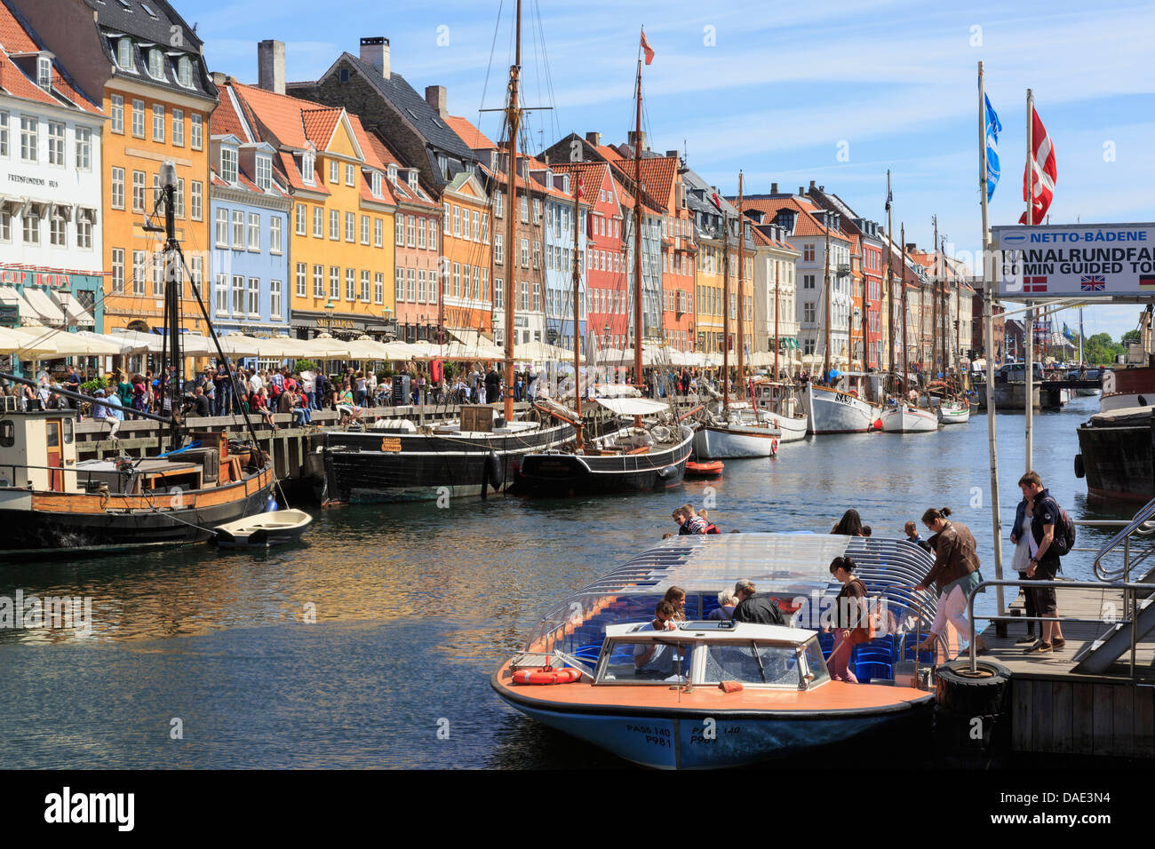 I turisti sul canal tour in barca con vecchie barche ormeggiate di fronte gli edifici colorati nel porto di Nyhavn a Copenaghen Zelanda Danimarca Foto Stock