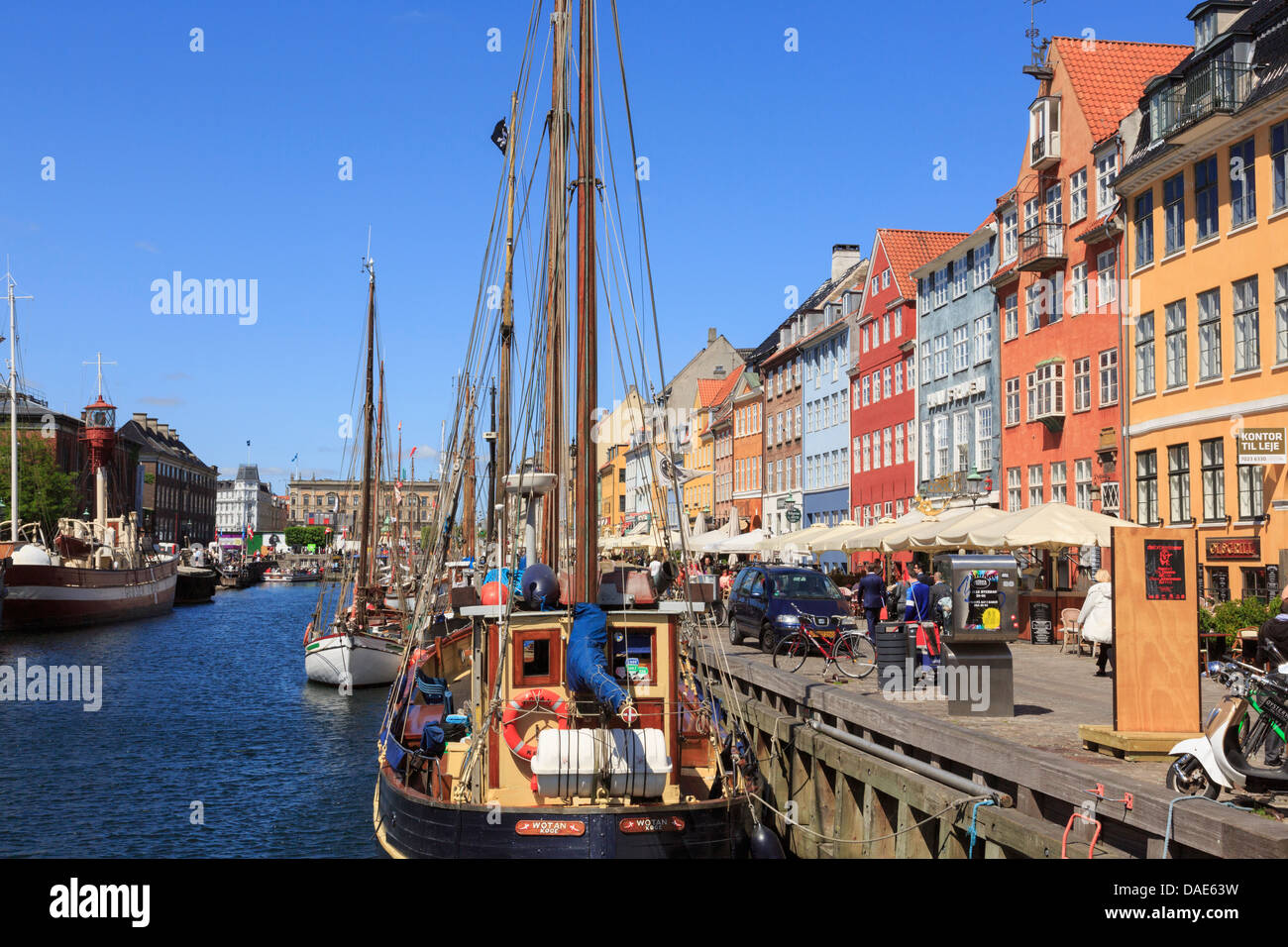 Vecchie barche ormeggiate sul canal con caffè e gli edifici colorati sul seicento lungomare nel porto di Nyhavn Copenhagen DANIMARCA Foto Stock