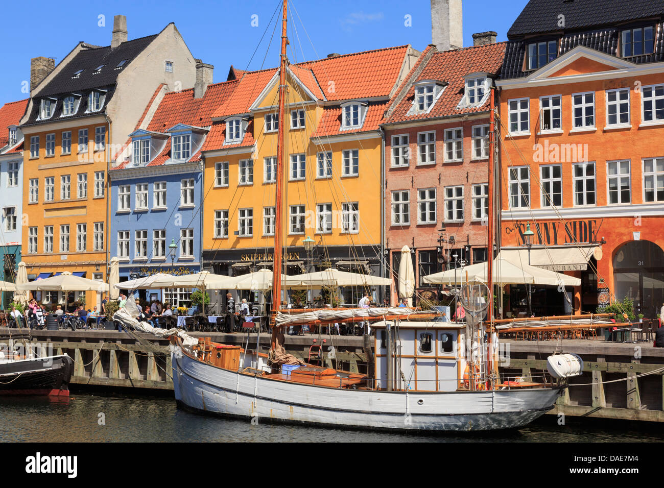 Vecchia barca in legno sul canal con caffè e gli edifici colorati sul seicento lungomare nel porto di Nyhavn Copenhagen DANIMARCA Foto Stock