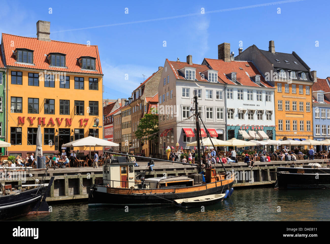 Vecchie barche di legno ormeggiate sul canal da colorati del xvii secolo edifici sul lungomare occupato con persone in Nyhavn Copenhagen DANIMARCA Foto Stock