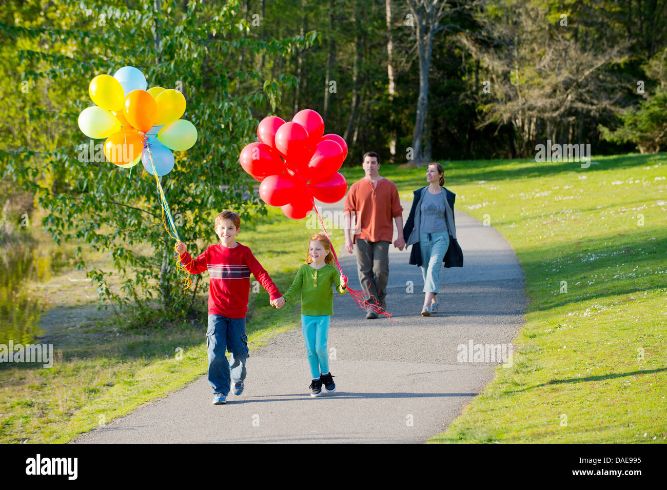 Famiglia a piedi attraverso il parco con grappoli di palloncini Foto Stock
