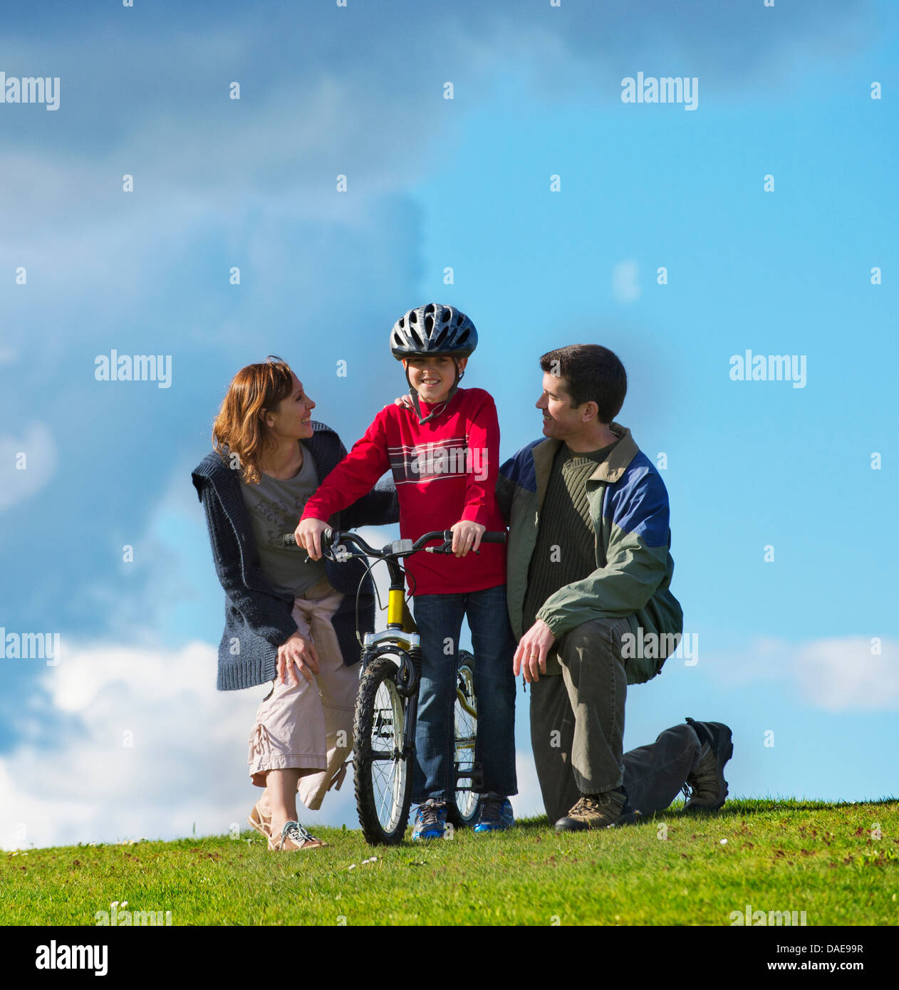 La madre e il padre il figlio incoraggianti per guidare la bicicletta Foto Stock