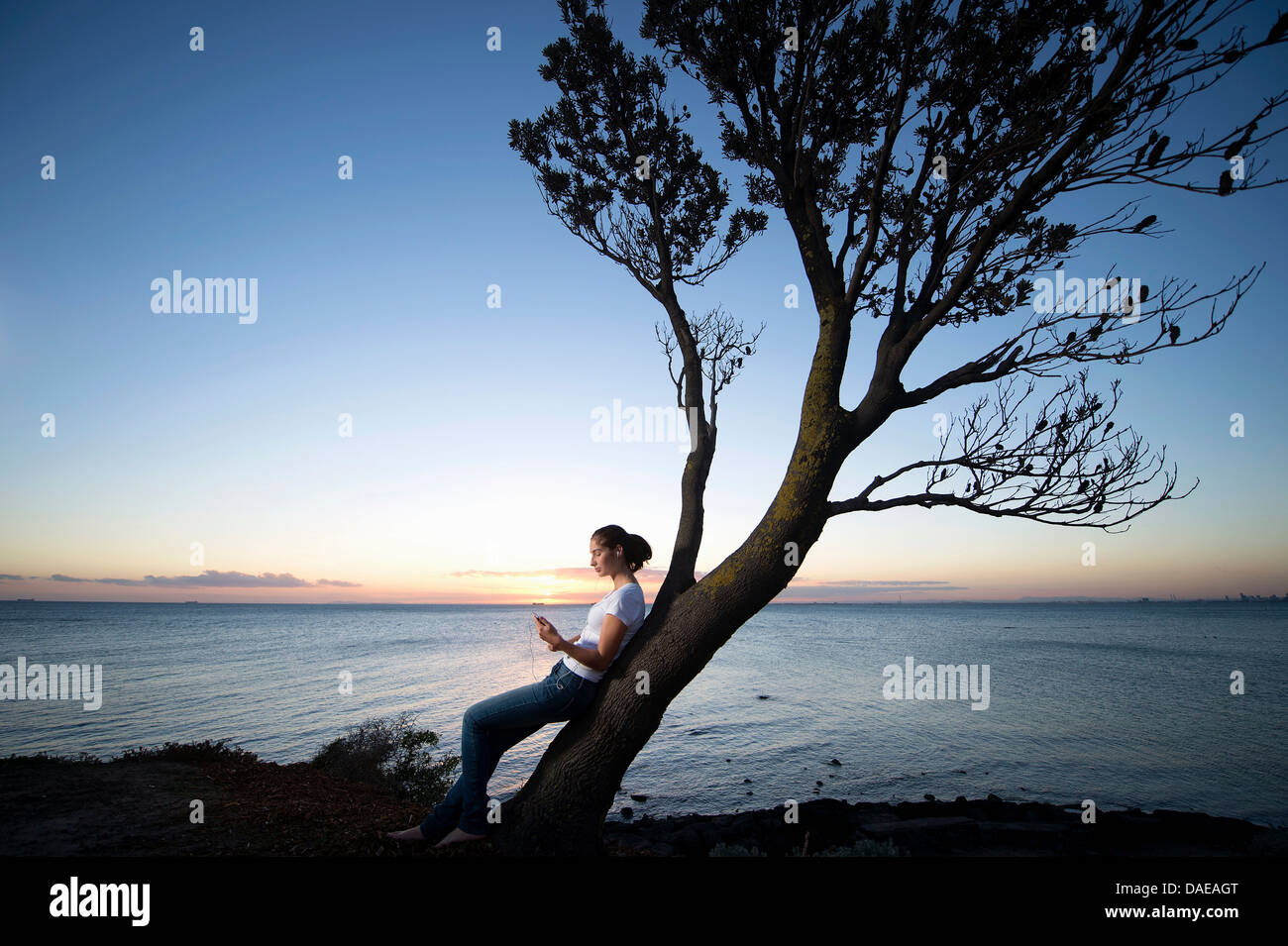 Giovane donna appoggiata su albero al tramonto Foto Stock