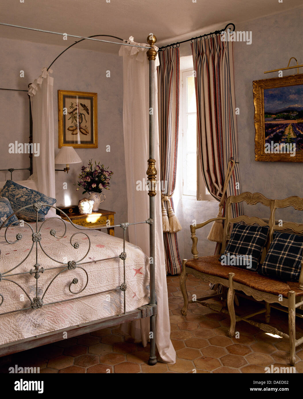 Antico metallo battuto letto con drappi bianchi nel paese francese camera da letto con rush seduto con divano blu cuscini controllati Foto Stock