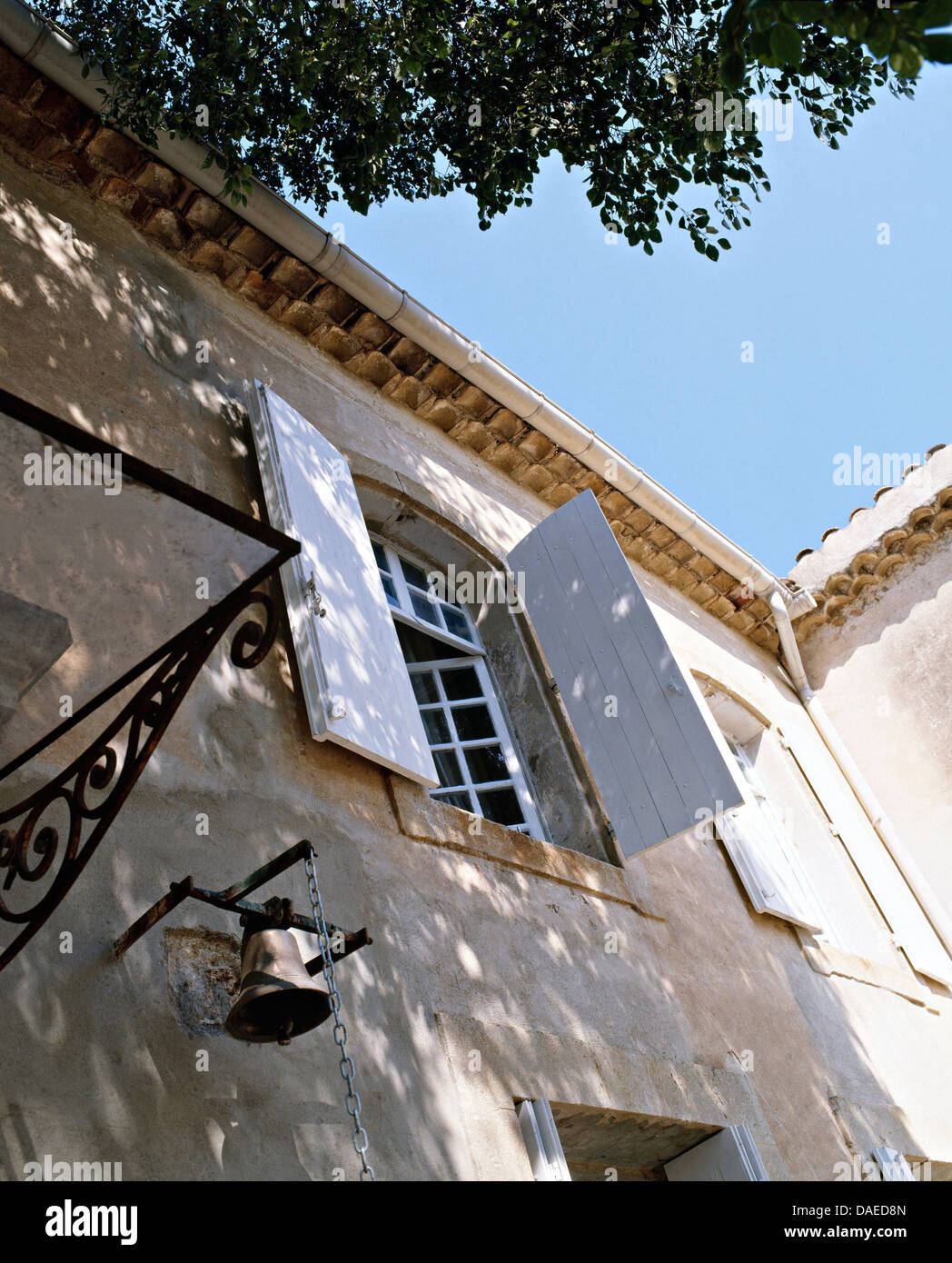 Dipinto di bianco di otturatori sulla finestra della casa francese di campagna con campana grande sulla parete Foto Stock
