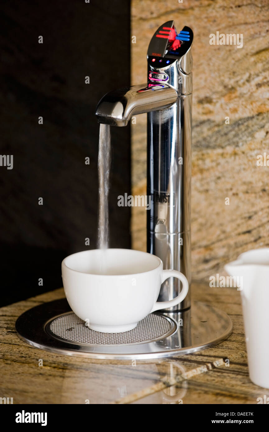 Acqua calda versando in tazza bianca da automatico acqua calda erogatore impostato nel piano di lavoro della cucina Foto Stock