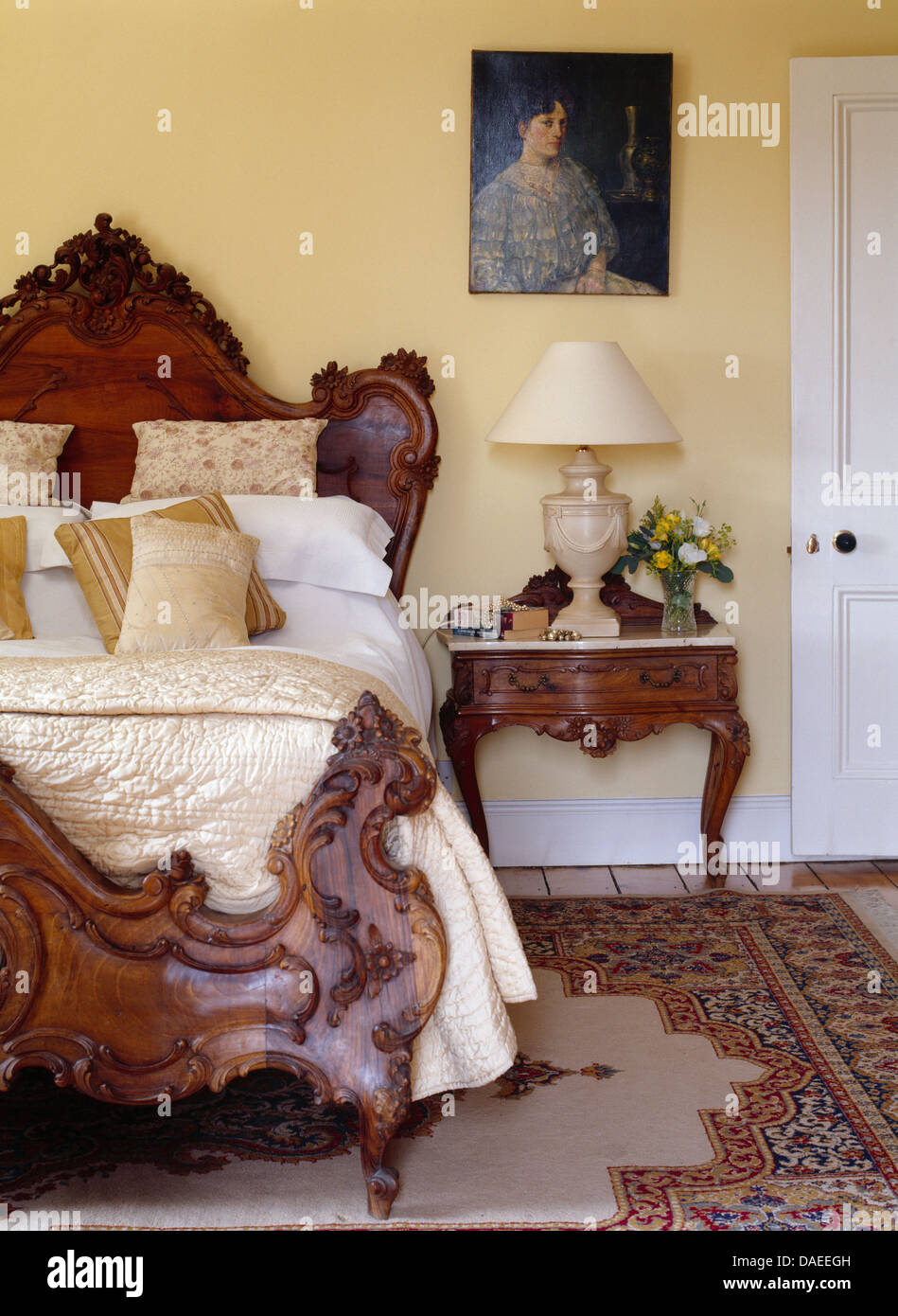 Letto antico con crema seta piumone e cuscini in paese tradizionale camera da letto con ritratto sulla parete sopra il comodino Foto Stock