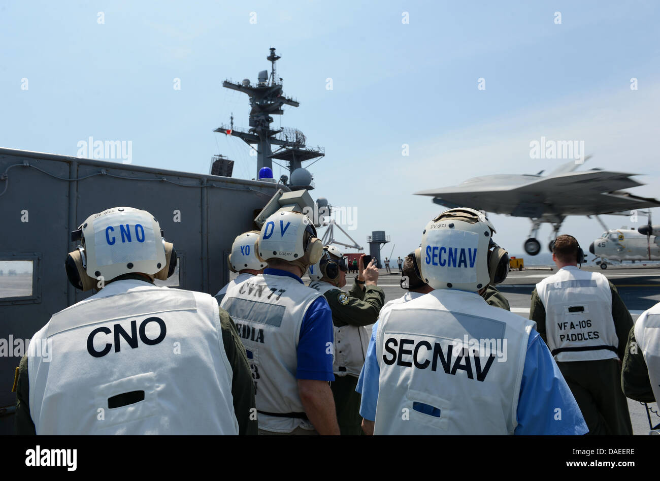 Capo di operazioni navali Adm. Jonathan Greenert, sinistra e segretario della Marina Ray Mabus guardare un US Navy X-47B Unmanned Combat Air System drone fare un arrestato atterraggio sul ponte di volo della portaerei USS George H.W. Bush Luglio 10, 2013 operanti nell'Oceano Atlantico. Lo sbarco ha segnato la prima volta che un velivolo senza equipaggio completato un arrestato in atterraggio a mare. Foto Stock