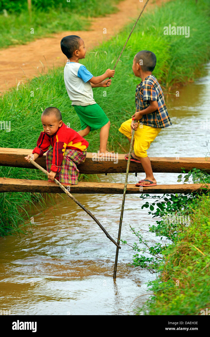 Tre ragazzi piccoli giocando su una passerella provvisorio oltre ad un ruscello vicino Lago Inle, Birmania Foto Stock