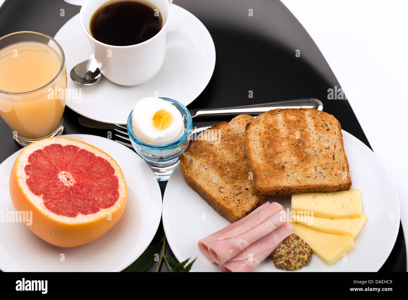 La prima colazione con pane tostato, prosciutto, formaggio, uova, succo di pompelmo, succo di frutta e caffè. Foto Stock