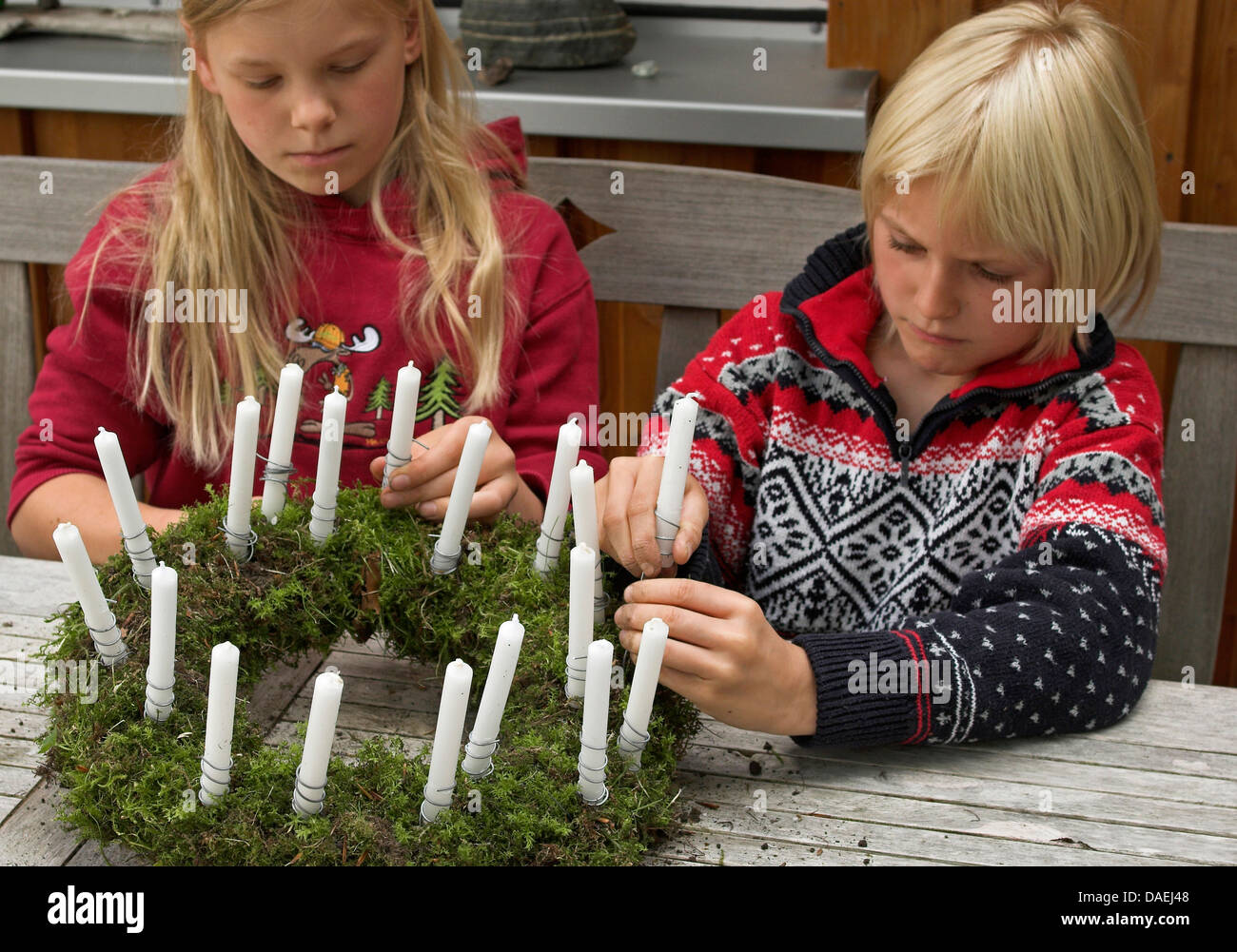 Bambini grippaggio candele su una corona di fiori per il tempo di Avvento, Germania Foto Stock