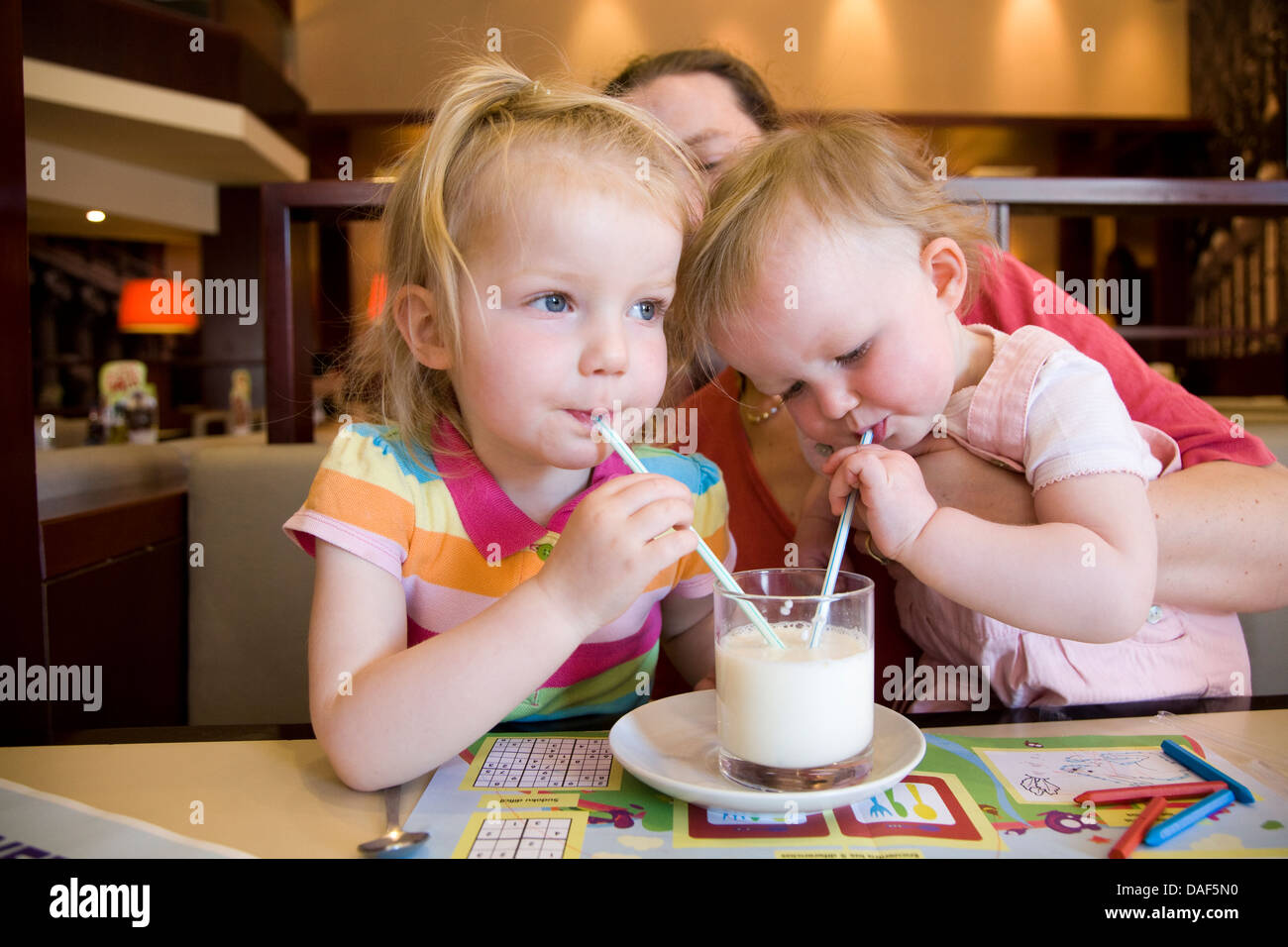 Due bambini 2 - Bimbo & baby - bere un bicchiere di latte di vacca con  cannuccia / cannucce, detenute da madre in un bar / ristorante Foto stock -  Alamy