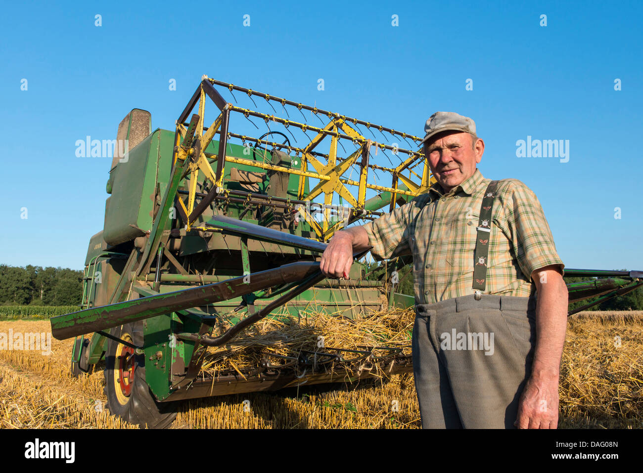 Il contadino di fronte al suo vecchio mietitrebbia nel campo di grano, Germania Foto Stock