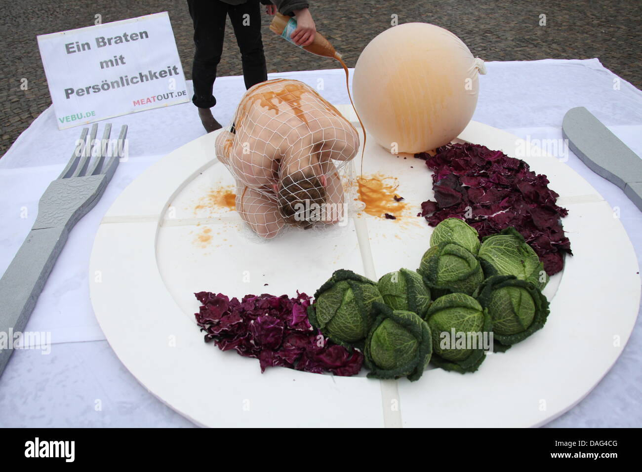 Un giovane uomo coperto in salsa giace su una piastra gigante con simbolici i cavoli di Bruxelles, gnocchi di patate e cavolo rosso presso la Porta di Brandeburgo a Berlino, Germania, 17 marzo 2011. Con questa azione di protesta, il tedesco alleanza vegetariano iniziato questo anno di giorni di azione della campagna internazionale Meatout. Foto: Emily Wabitsch Foto Stock