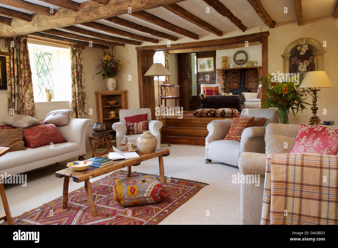 White divani e poltrone con rustici tavoli da caffè in legno con travi in cottage la stanza di seduta con il tappeto bianco Kelim rug Foto Stock