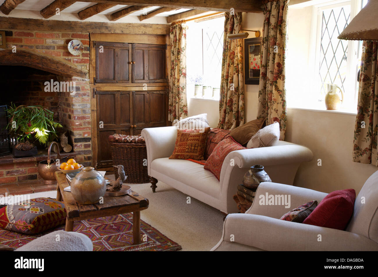 Divani bianchi accatastati con cuscini e rustico tavolo da caffè in legno in cottage in salotto con mattoni a vista camino Foto Stock