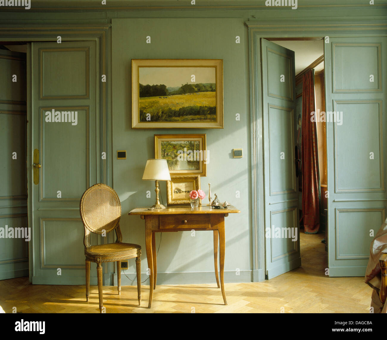 La pittura di paesaggio sulla parete sopra piccolo tavolo e una sedia antichi e grigio chiaro rivestite con pannelli di legno francese hall con metà aprire porte doppie Foto Stock