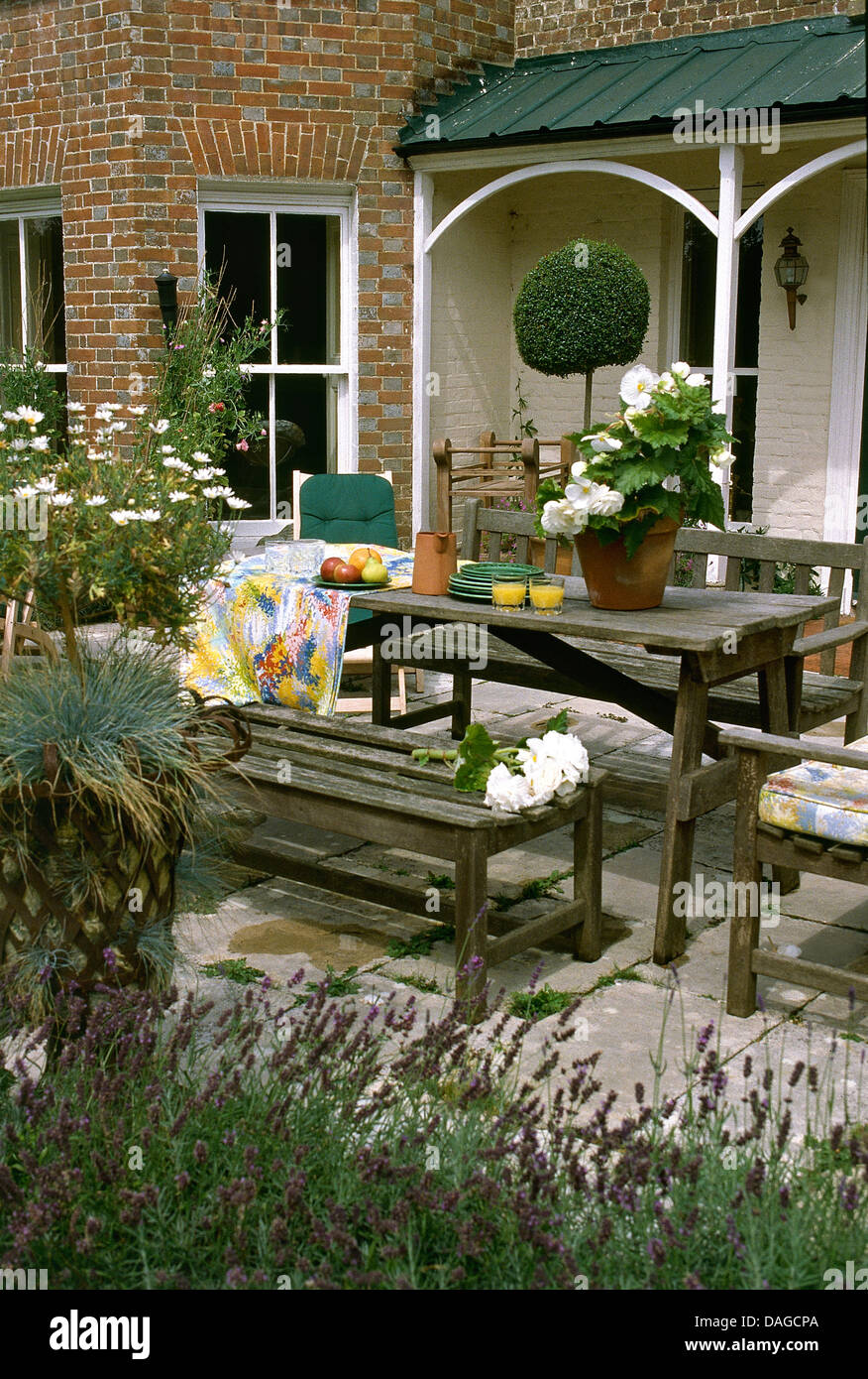 Panca in legno e tavolo con pentola di begonie bianco sulla pietra lastricata patio esterno casa vittoriana con veranda Foto Stock