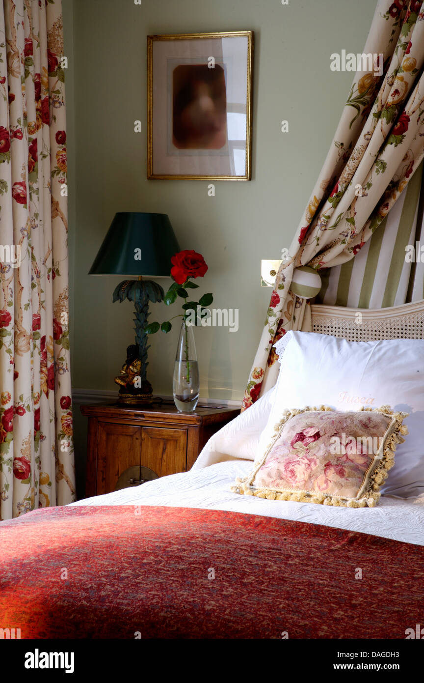 Tendaggi floreali sopra il letto con cuscini di colore bianco e rosso cover letto in colore verde pallido camera da letto con luce verde sul comodino Foto Stock