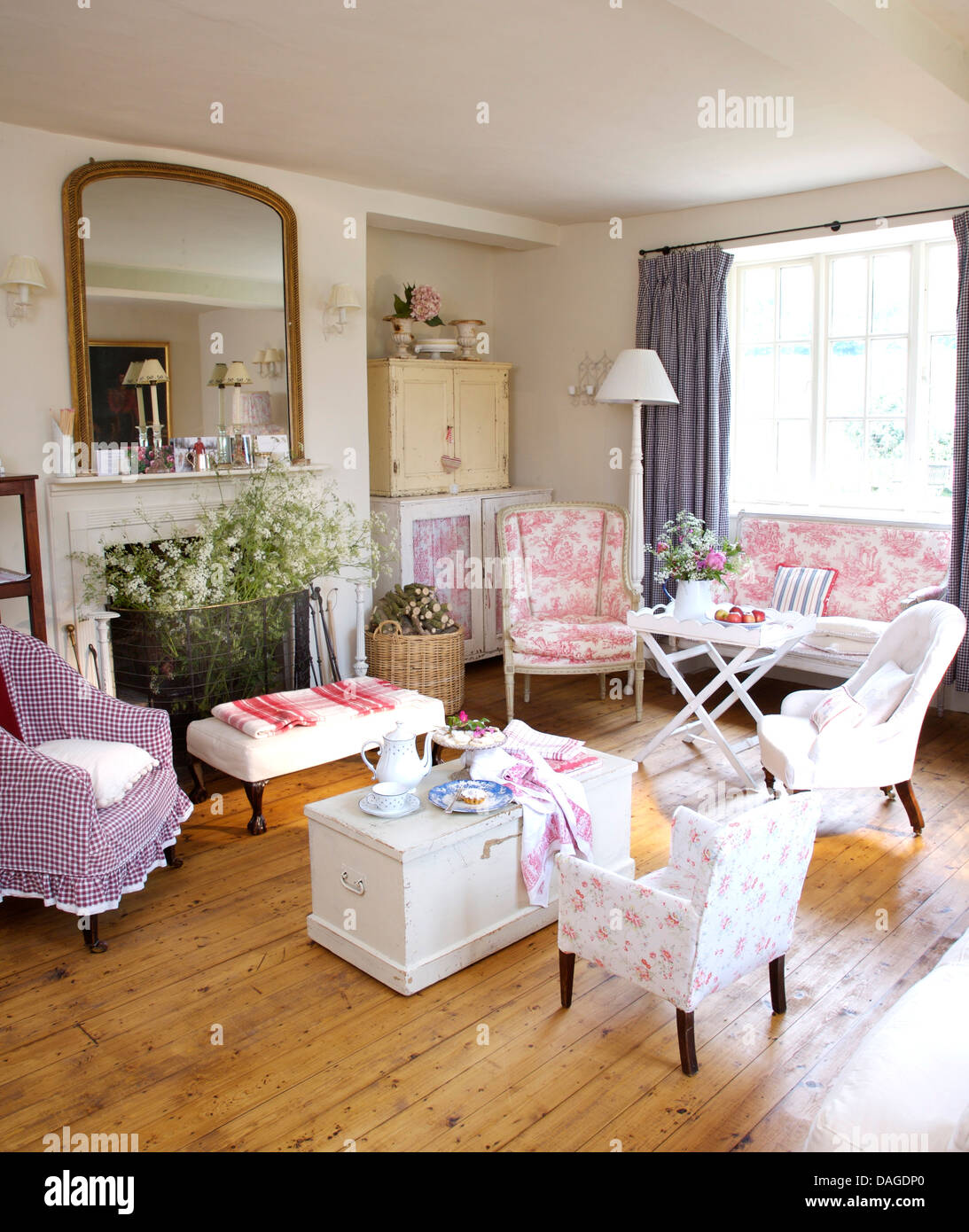 White cassa di legno con colori pastello e sedie e pavimento in legno cottage soggiorno con grande specchio sopra il camino Foto Stock