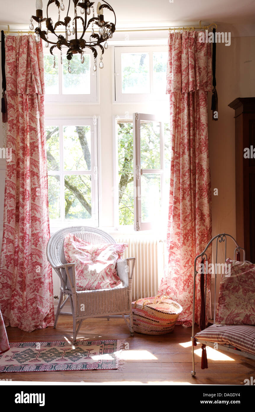 Dipinto di canna da zucchero sedia davanti alla finestra con il rosa Toile de Jouy tende in paese francese camera da letto Foto Stock