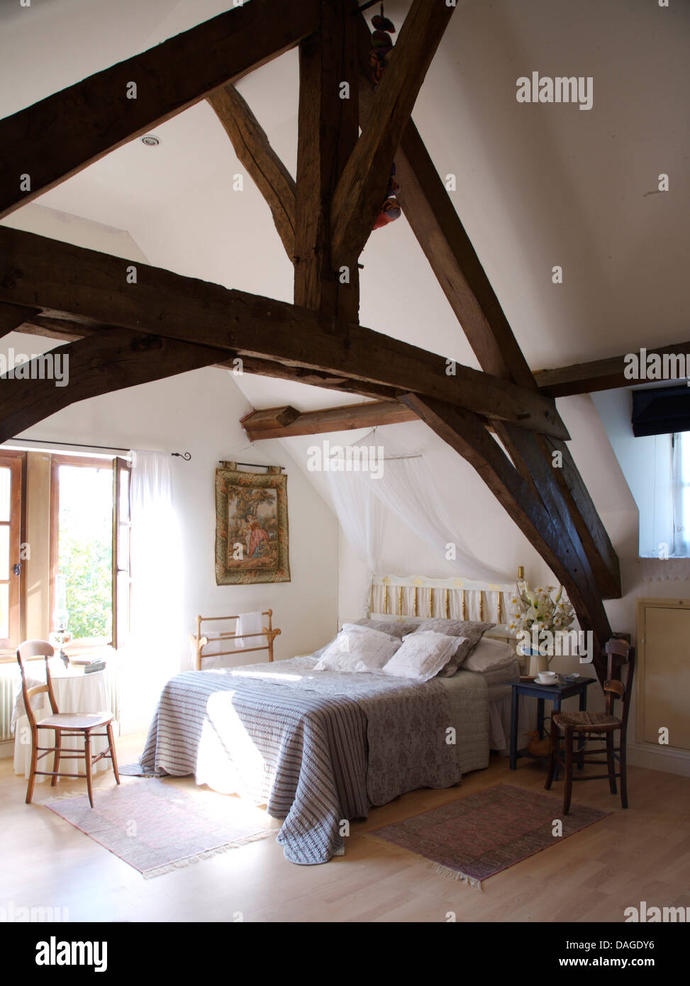 Rustiche travi di legno sul soffitto apex nel paese francese camera con coperchio blu sul letto matrimoniale Foto Stock
