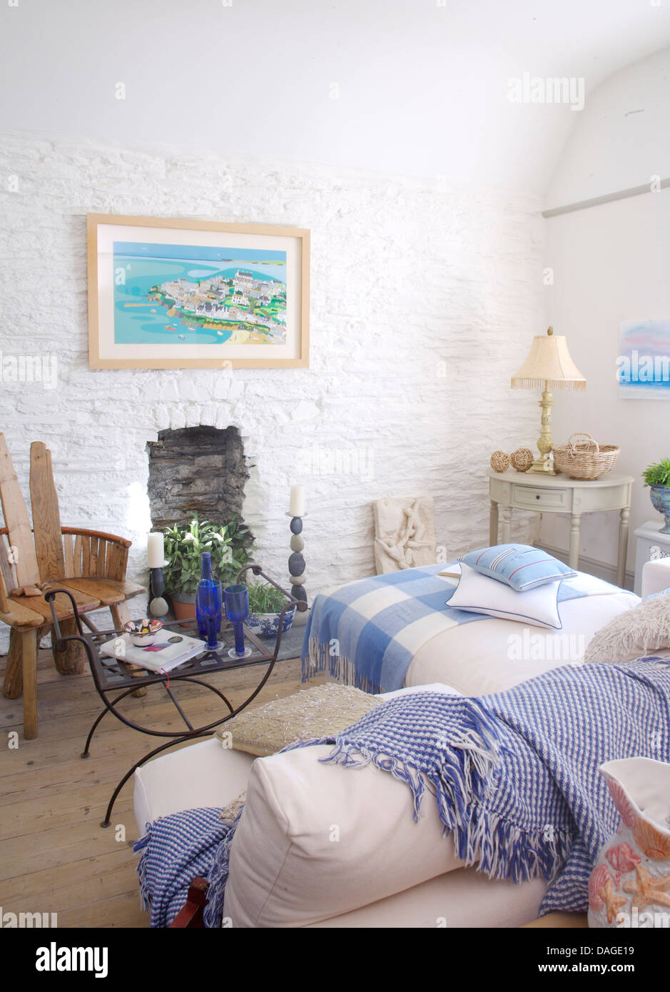 Controllare blu buttare sul divano bianco in bianco cottage soggiorno con dipinto di muri di pietra e controllato rug sulla chaise longue Foto Stock