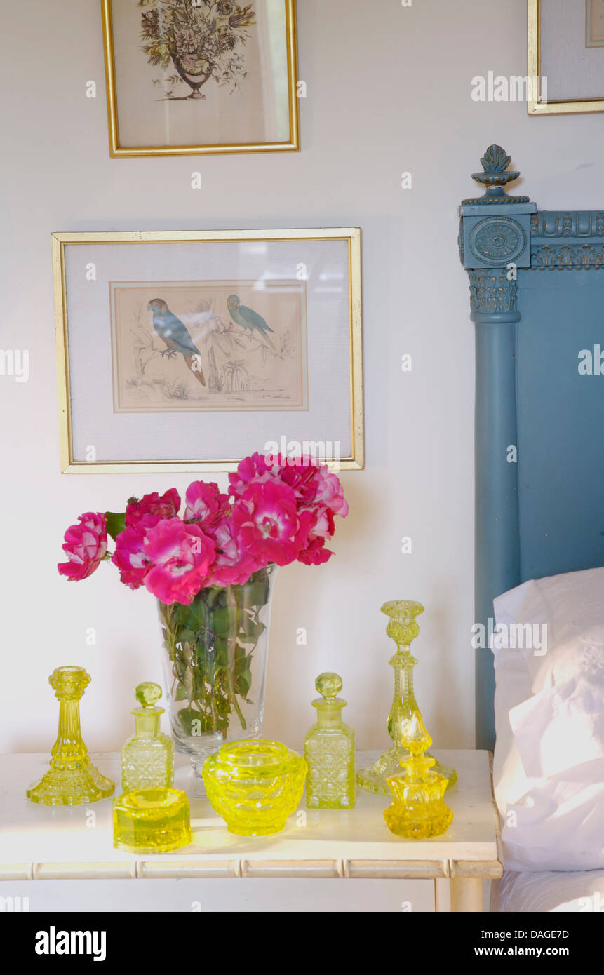 Raccolta di giallo vintage vetreria e vaso di rosa pilastro americano rose sul comodino in camera da letto del paese Foto Stock