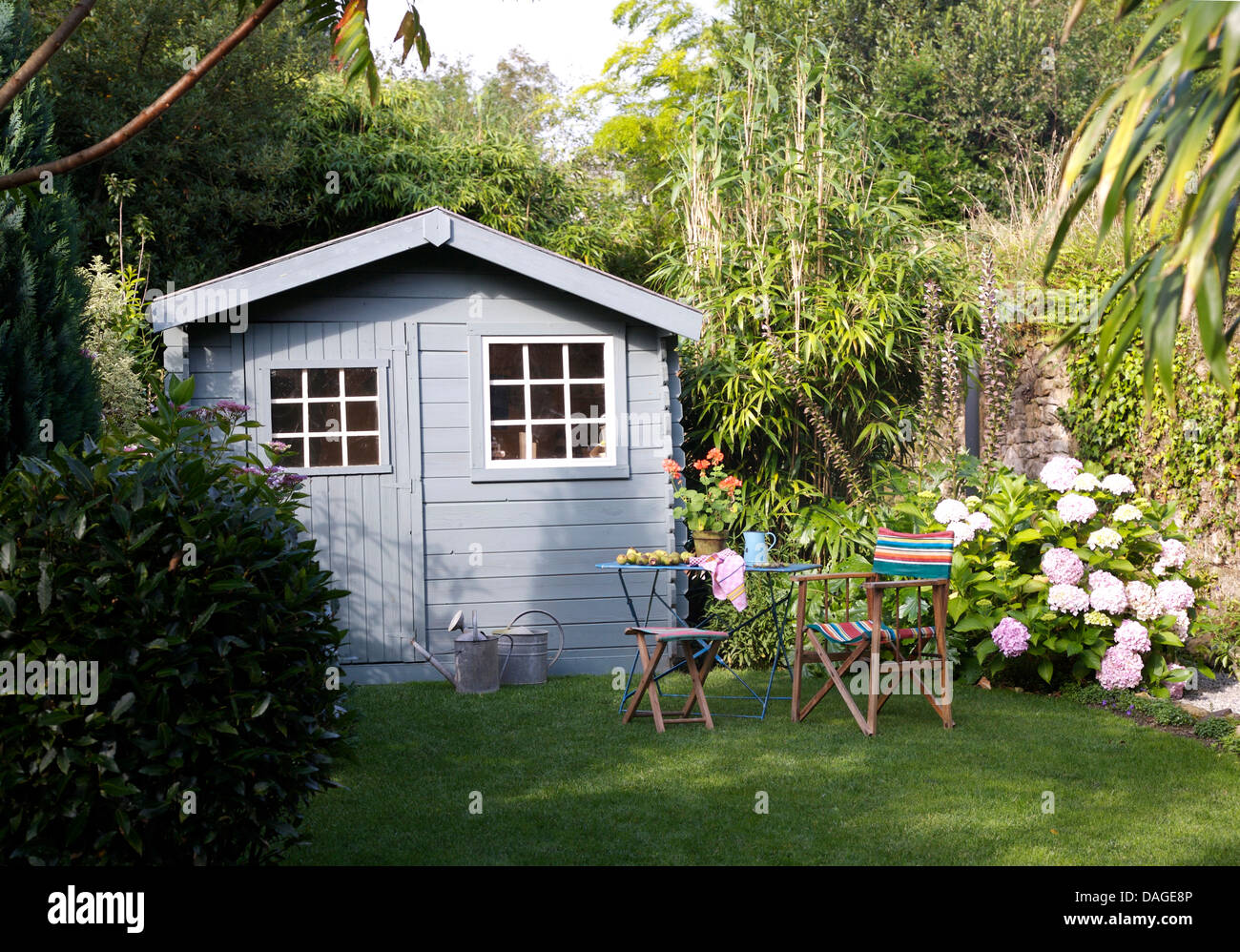 Tavolo e sedie sul prato di fronte blu pallido sparso nel paese francese giardino in estate con ortensie rosa contro la parete Foto Stock