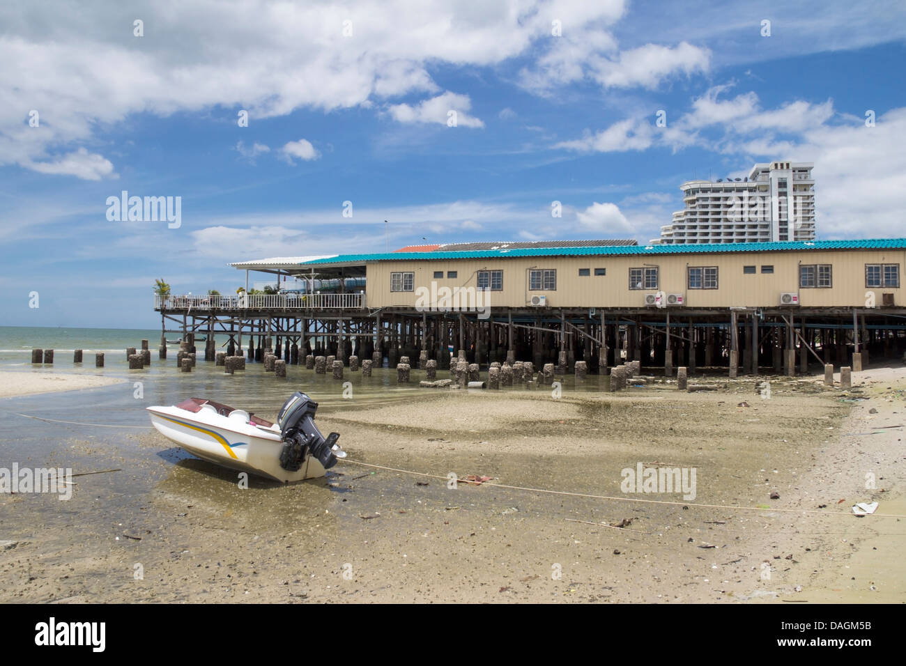 Barca con motore fuoribordo sulla spiaggia cittadina, ristorante Pier e Hilton hotel in background, Hua Hin, Thailandia Foto Stock