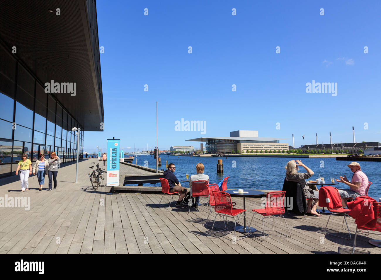 Persone in waterfront café fuori la Royal Danish Playhouse con la Opera House di tutta l'acqua. Copenaghen, Zelanda, Danimarca Foto Stock