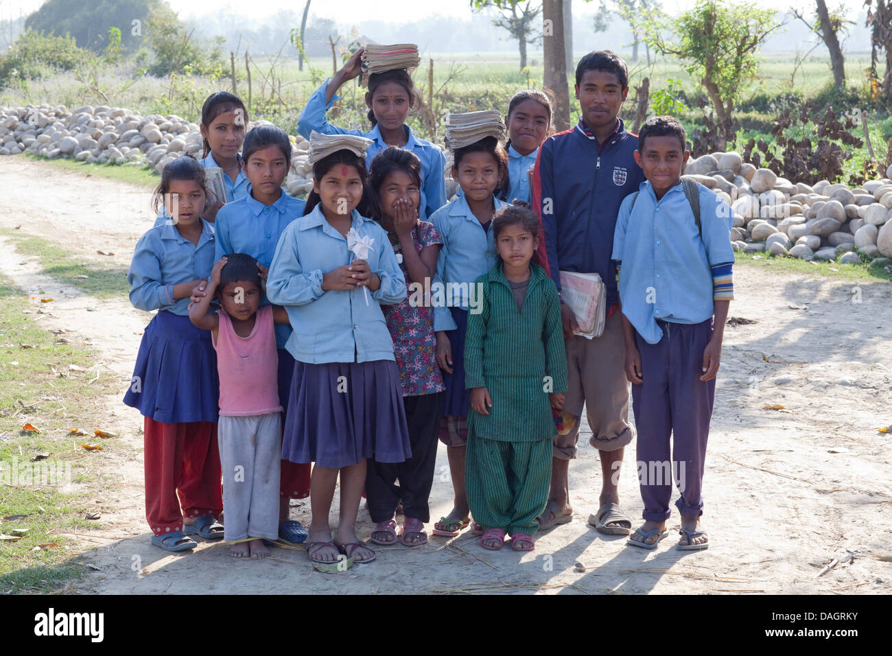 Tharu scolari, tre dei quali stanno portando i loro ben utilizzati libri bilanciato sulle loro teste. Bardia. Zona di Bheri. Terai. Il Nepal. Foto Stock