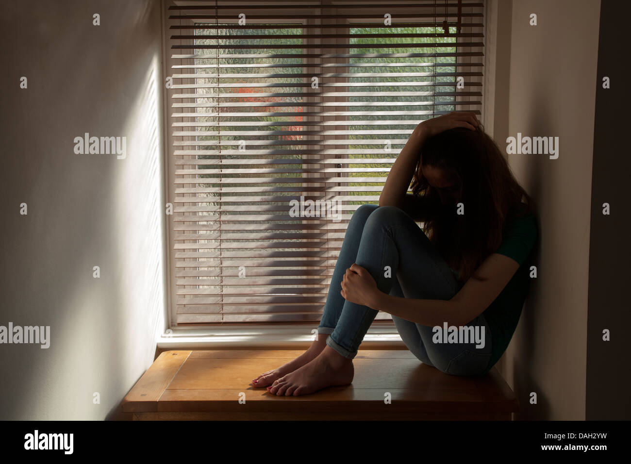 Una ragazza adolescente, la mano sulla sua testa, seduti in una finestra con una luce di colata. Modello di proprietà e rilasciato. Foto Stock
