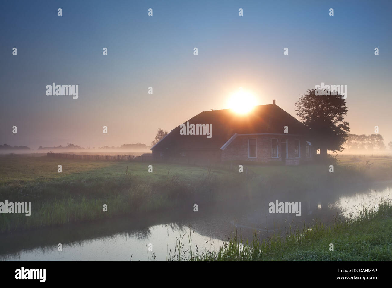 Raggi di sole su casa colonica nella nebbia di mattina Foto Stock