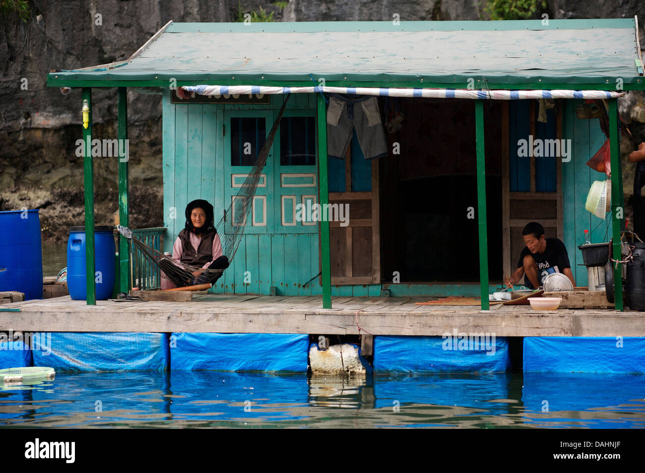 Il vietnamita casa galleggiante con la donna in amaca e uomo di mangiare, Halong Bay, Vietnam Foto Stock