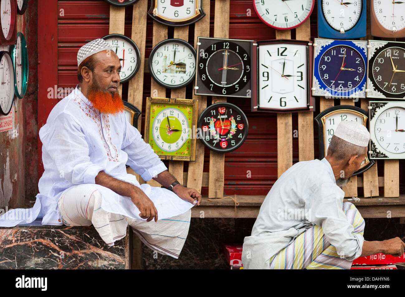 Un uomo musulmano con la sua barba tinta rosso con Henna vende orologi al suo stallo nella storica città vecchia di Dacca in Bangladesh Foto Stock