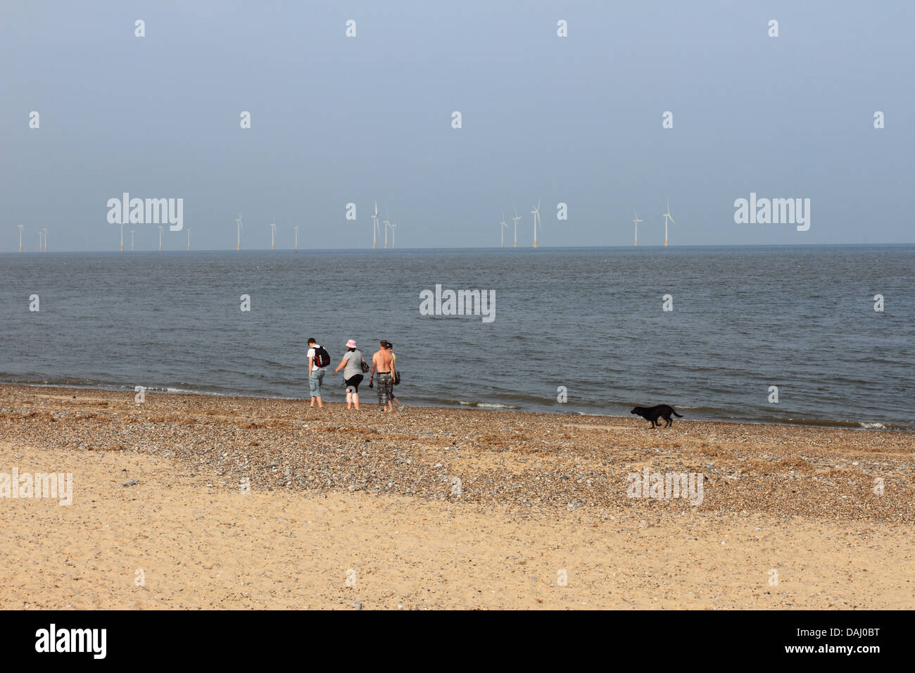 La gente cammina sulla spiaggia, Holiday Makers godendo sulla grande spiaggia di Yarmouth, Scroby turbina eolica sul retro, Norfolk, Regno Unito Foto Stock