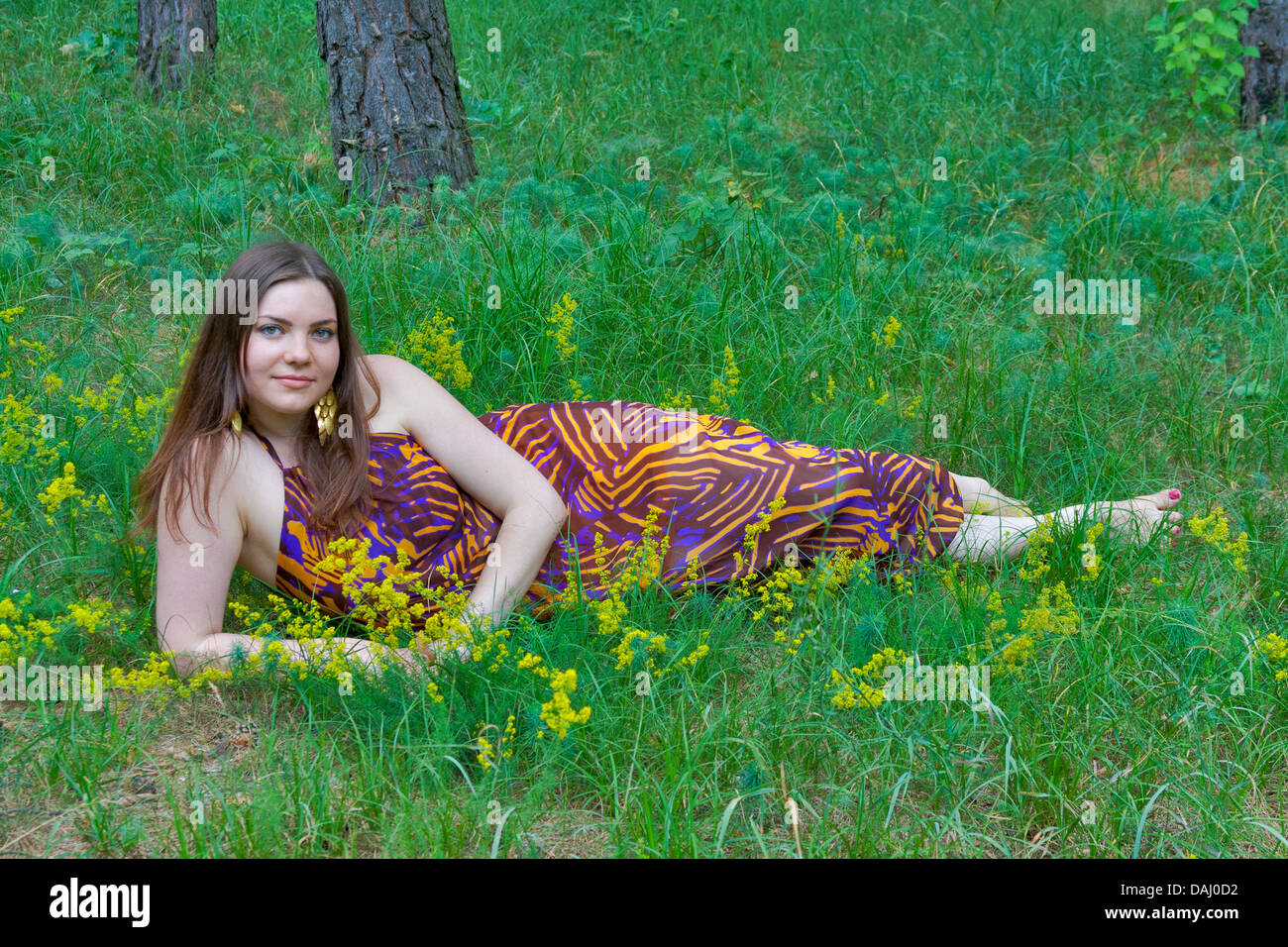 Giovane donna graziosa con bouquet di fiori selvatici che giace nella foresta Foto Stock