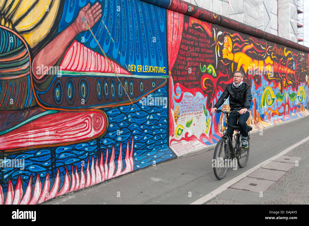 Ciclista passa dalla East Side Gallery, il muro di Berlino (Berliner Mauer), Germania Foto Stock