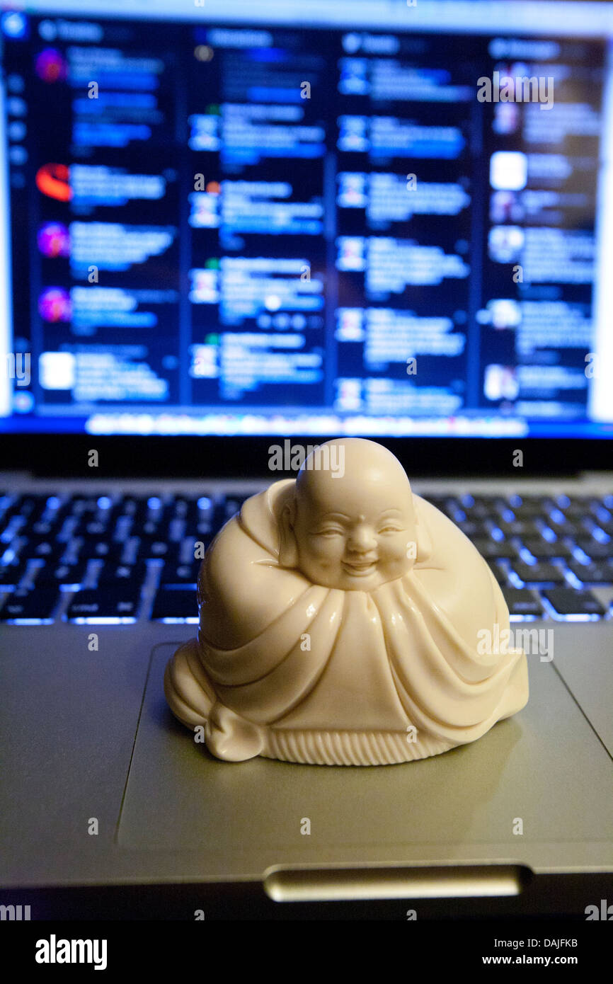 Piccolo Buddha buddista statua in ceramica sat su Apple Power Book con ridacchiando Tweetdeck in background Foto Stock