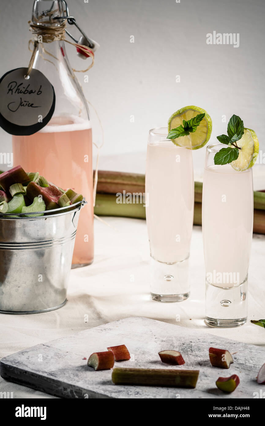 Pezzi di rabarbaro sul tagliere con vetro e una bottiglia di succo di rabarbaro Foto Stock