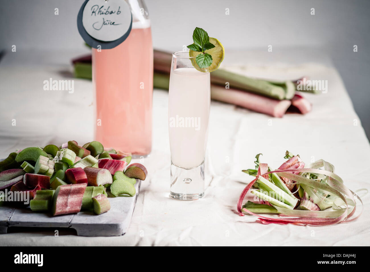 Pezzi di rabarbaro sul tagliere con vetro e una bottiglia di succo di rabarbaro Foto Stock