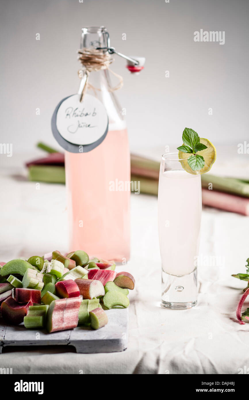 Pezzi di rabarbaro sul tagliere con vetro e una bottiglia di succo di rabarbaro Foto Stock