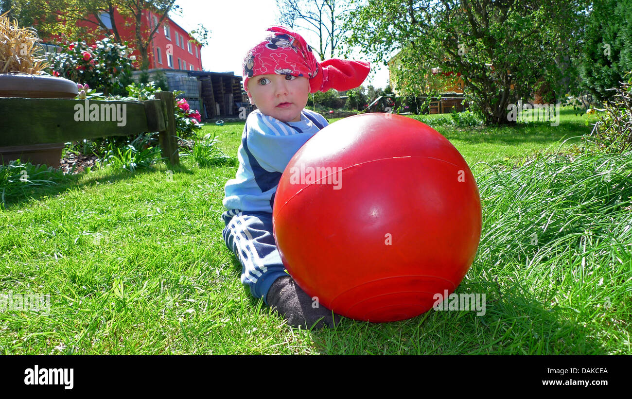 Bambino seduti in giardino nel prato e giocare con una palla di luppolo, Germania Foto Stock